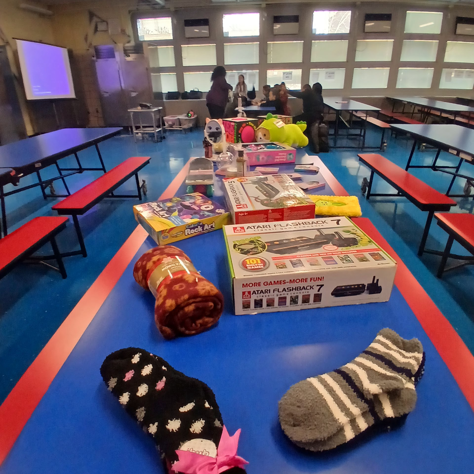 Tables of toys, blankets, and gifts set up inside a school cafeteria